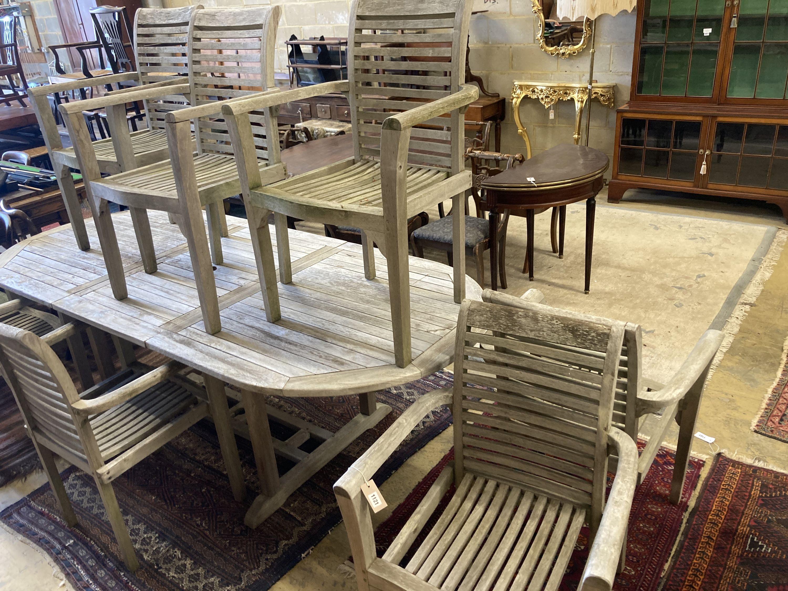 A weathered teak extending garden table, length 240cm extended, depth 100cm, height 77cm together with a set of seven weathered teak elbow chairs